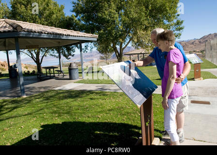 Caucasian Senior Couple (età 60-70) leggere il cartello di informazione a Hemingway Park Boulder City Nevada USA. L'uomo ha un braccio intorno alla vita della donna. Foto Stock