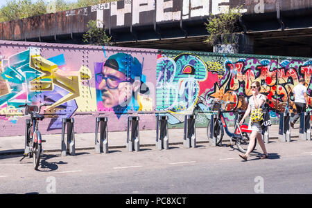 Street View di Brick Lane con la giovane donna a piedi. Street Art graffiti murali in background. Brick Lane, Shoreditch, London, Regno Unito Foto Stock