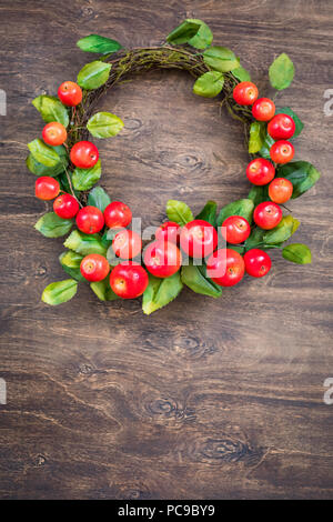 Una corona di fiori colorati di piccole mele rosse sullo sfondo di legno Foto Stock