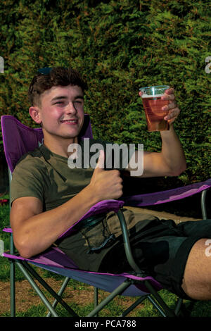 Giovane adulto seduto fuori godendo il sole estivo con una birra in un giardino Foto Stock