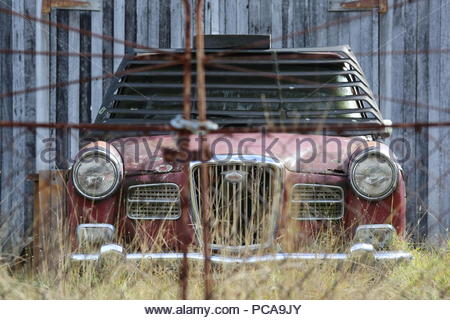 Una vecchia ruggine auto inutilizzati si erge come l'erba cresce attorno ad esso in prossimità di una casa diroccata. Foto Stock