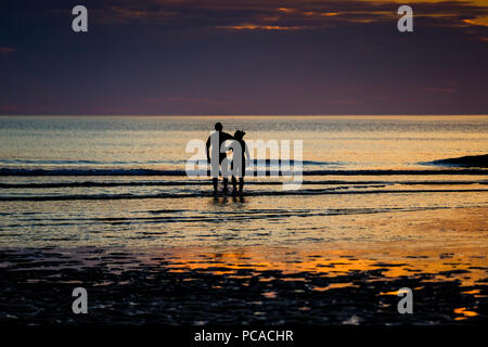 Matura in piedi sul Porth Beach a Newquay in Cornovaglia, guardando al mare come il sole scende Foto Stock