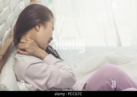 Donna asiatica dolore al collo dopo svegliarsi la mattina sul letto in camera da letto Foto Stock