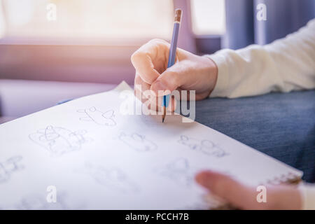 La donna esegue a mano libera il disegno a matita le opere su carta bianca in morbide tonalità di luce calda dalla finestra. Foto Stock