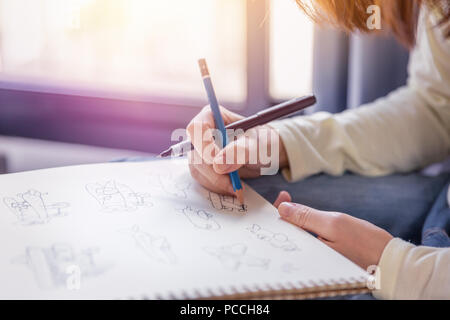 La donna esegue a mano libera il disegno di opere d'arte con la penna e matita su carta bianca in morbide tonalità di luce calda dalla finestra. Foto Stock