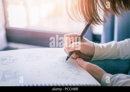 La donna esegue a mano libera penna inchiostro disegno le opere su carta bianca in morbide tonalità di luce calda dalla finestra. Foto Stock