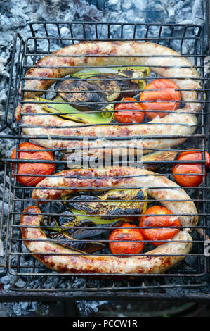 Salsicce di maiale con verdure alla griglia sul fuoco. Cucinare la cena all'aperto. Foto Stock