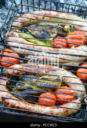 Salsicce di maiale con verdure alla griglia sul fuoco. Cucinare la cena all'aperto. Foto Stock