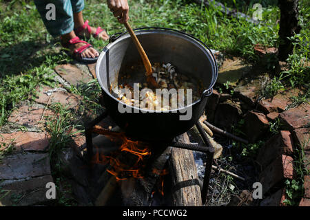 Donna agitazione in una ghisa calderone dove uno stufato di gulasch è in ebollizione, oltre il caminetto aperto nel cortile di una casa rurale in Romania Foto Stock