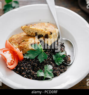 Chiudere la piastra di supporto con il nero di quinoa e costolette di fiocchi d'avena con prugne su un tavolo di legno. Cena vegetariana tabella Foto Stock