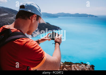 Uomo a catturare fotografia di myrtos costiera paesaggio del mare. Il blu ciano superficie di acqua con isola forma, Cefalonia, Grecia. Foto Stock