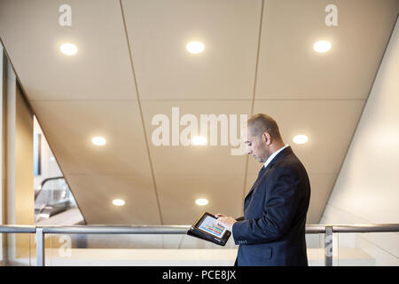 Un medio orientali imprenditore lavora su un computer portatile in piedi in un ufficio lobby. Foto Stock