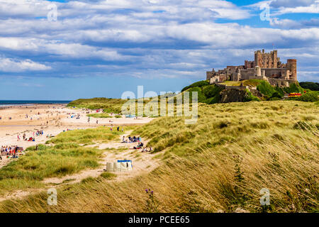 Il castello di Bamburgh e la spiaggia su una trafficata soleggiata giornata estiva, Bamburgh, Northumberland, Regno Unito. Luglio 2018. Foto Stock