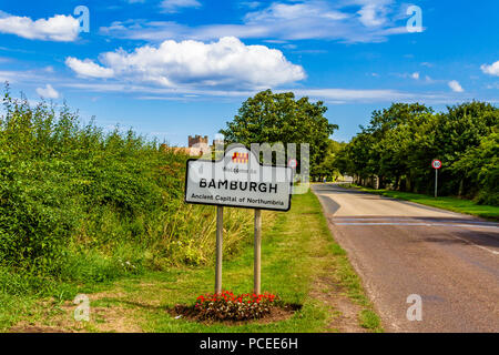 Segno accogliente gli automobilisti a Bamburgh village, con il castello di Bamburgh in background. Bamburgh, Northumberland, Regno Unito. Foto Stock