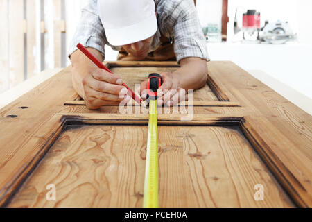 Carpenter al lavoro le misure con il metro a nastro e matita su uno sfondo di legno Foto Stock