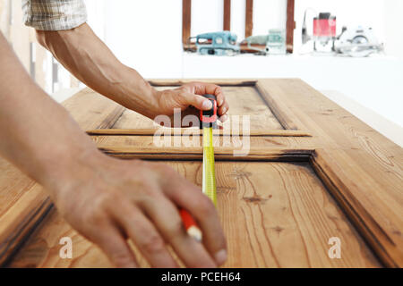 Carpenter al lavoro le misure con il metro a nastro e matita su uno sfondo di legno Foto Stock