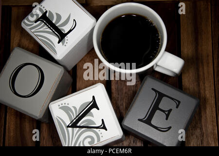 La parola amore con una tazza di caffè in un cerchio al buio su un sfondo di legno Foto Stock