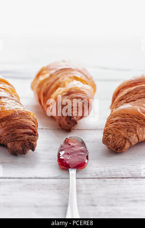 Tre i croissant su un bianco tavolo in legno con cucchiaino riempita con marmellata al centro Foto Stock