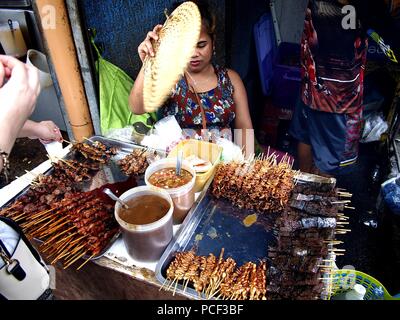ANTIPOLO City, Filippine - 30 luglio 2018: una donna vende un assortimento di carne di maiale alla griglia e interiora di pollo su un bastone nel suo cibo stallo. Foto Stock