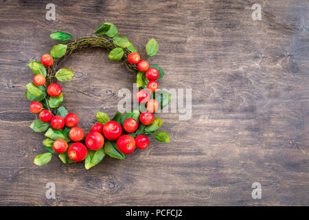 Una corona di fiori colorati di piccole mele rosse sullo sfondo di legno Foto Stock