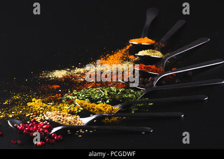 Composizione di piccoli cucchiai colmi di spezie e condimenti per la cottura su sfondo nero Foto Stock