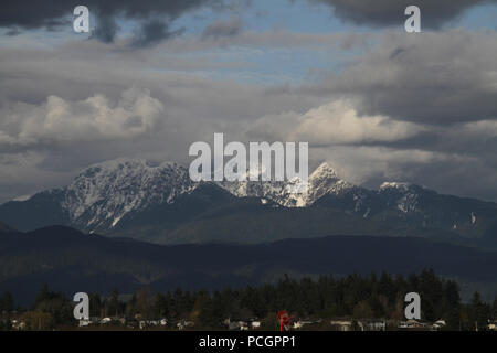 Cime innevate dietro una foresta e colline Foto Stock