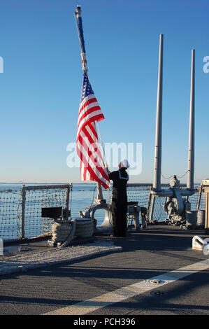 NORFOLK (dec. n. 14, 2012) marinaio reclutare Guillermo Garciavillareal regola il ensign nazionale sul ponte di volo dell'guidato-missile destroyer USS Barry (DDG 52) a metà-montante in ricordo delle vittime e le famiglie interessate dal 14 dicembre le riprese a Sandy Hook Scuola Elementare di Newtown, Conn. Il presidente Barack Obama ha ordinato le bandiere degli Stati Uniti per essere volato a metà personale venerdì per onorare le vittime della massa di ripresa. Foto Stock