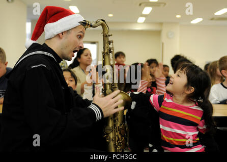 YOKOSUKA, Giappone (dec. n. 3, 2012) musicista di terza classe Brandon Kiesa, membro dell'U.S. 7 Flotta Estremo Oriente Edition Brass Band, mostra un bambino il sassofono durante un Natale in musica le prestazioni al Sullivans Scuola elementare a comando le attività della flotta, Yokosuka. La band ha suonato brani musicali in diverse ubicazioni in tutto il giorno anche il bambino Centro di sviluppo e al di fuori del Navy Exchange. Foto Stock