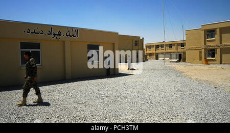 A Kandahar, Afghanistan - Un esercito nazionale afghano Air Corps (ANAAC) soldato passeggiate sulla recentemente costruita ANAAC camp adiacente a Kandahar Air Field. Edifici sul campo display messaggi di ispirazione per i soldati, scritto in dari. Il messaggio mostrato su un edificio a sinistra letture, Allah, Hewad, Dandah", il che si traduce in "Dio, Paese lavoro." i piloti e i membri dell'equipaggio di ANAAC sono addestrati e consigliato dal combinato di alimentazione Aria forza di transizione, la capacità aria elemento di formazione della NATO Training Mission - Afghanistan (NTM-A), con sede a Camp Eggers a Kabul. NTM-A livello regionale i team di supporto Foto Stock