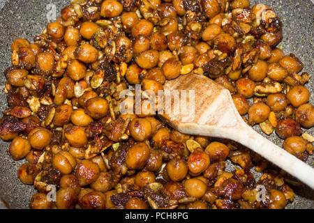 La tostatura gustoso croccante di ceci e semi in una padella con un cucchiaio di legno.jpg Foto Stock