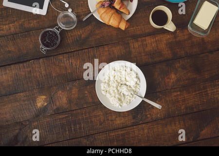 Colazione sana nozione. Piatto di formaggio fresco, croissant, burro, caffè e marmellata sul tavolo di legno Foto Stock