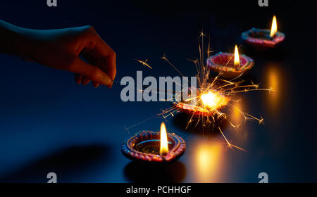 Felice Diwali - Illuminazione un sparkler con lampada diya Foto Stock