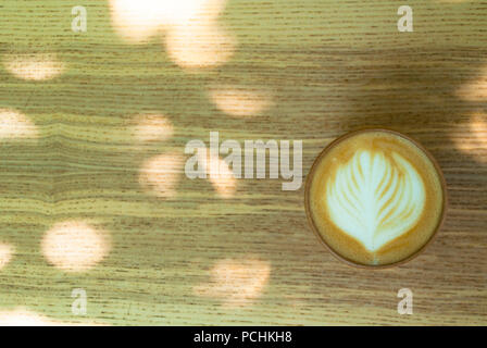 Una tazza di cappuccino fresco con belle latte art naturale sul tavolo di legno in un albero ombra. Foto Stock