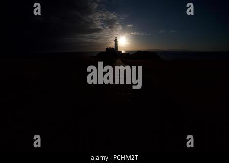 Silhouette di un faro (Turnberry Faro) lungo la costa dell'Ayrshire accanto al Trump Turnberry Golf, con il tramonto in background. Foto Stock