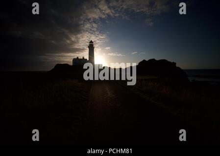 Silhouette di un faro (Turnberry Faro) lungo la costa dell'Ayrshire accanto al Trump Turnberry Golf, con il tramonto in background. Foto Stock