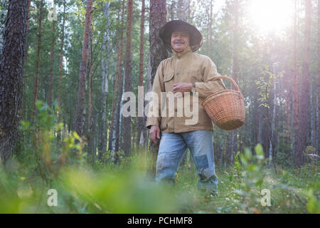 Uomo maturo picking camminare con il cestello nella foresta. Egli si sta guardando attorno godendo l'aria fresca del legno. Foto Stock