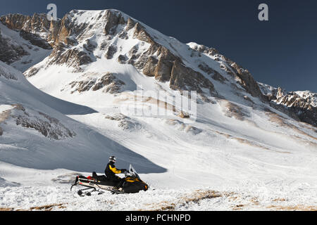 Un uomo su una motoslitta contro uno sfondo di cime innevate. Riserva naturale statale di Adygea, Russia. Foto Stock