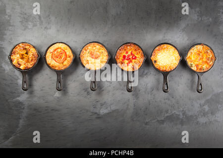 Sei singoli mini quiche torte in ghisa pentole al buio su un superficie di ardesia Foto Stock