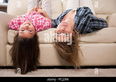 Bella madre con sua figlia carino sdraiato sul lettino con la loro testa a testa in giù a sorridere e ridere. Trascorrere del tempo di qualità insieme Foto Stock