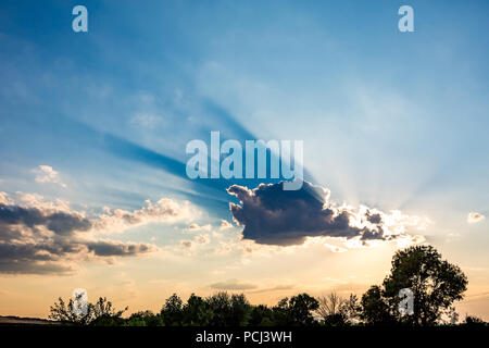 Colorato tramonto cielo con le nuvole e il sole sembra scoppiare fuori da dietro di loro gettando bella blu cast. Alcuni alberi nella parte anteriore. Bulgari Foto Stock