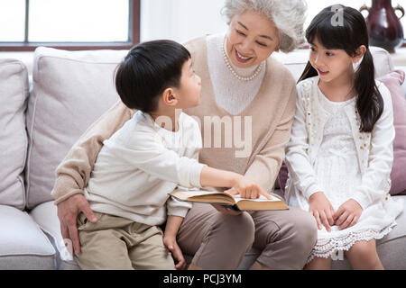 Allegro nonna cinese e i nipoti la lettura di un libro sul divano Foto Stock