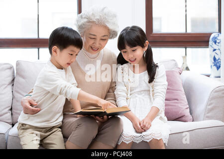 Allegro nonna cinese e i nipoti la lettura di un libro sul divano Foto Stock