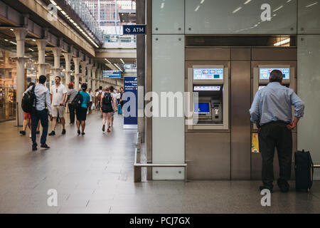 Uomo che utilizza un ATM dentro la stazione di St. Pancras, London, Regno Unito, gente camminare passato. Foto Stock