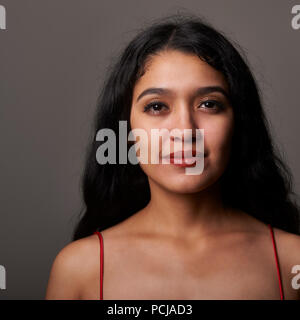 Studio portrait session di 17 anni ragazza adolescente che indossa un abito rosso su sfondo grigio Foto Stock