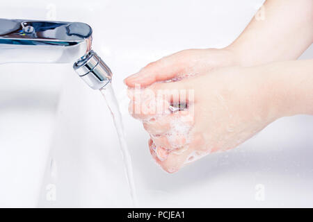 Femmina insaponato le mani su un bacino pronto a lavare sotto l'acqua corrente Foto Stock