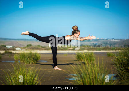 Donna sulla spiaggia Los Lances facendo warrior III Yoga posa, lo stretto parco naturale, Tarifa, Cadice, Andalusia, Spagna Foto Stock