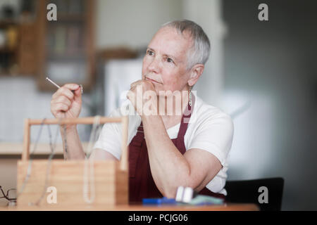 Donna seduta al tavolo che fissa una collana Foto Stock