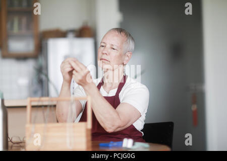 Donna seduta al tavolo che fissa una collana Foto Stock