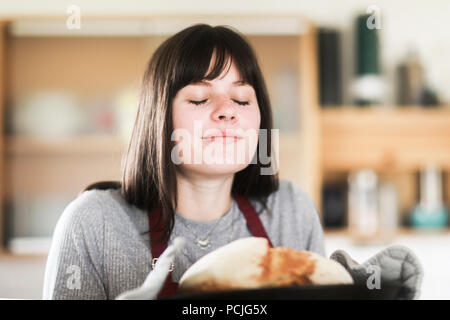 Donna sorridente in piedi in cucina tenendo un pane appena sfornato pagnotta di pane Foto Stock