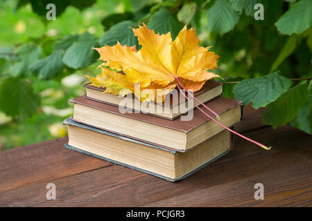 Libri antichi giallo con foglie di acero su un tavolo rustico Foto Stock